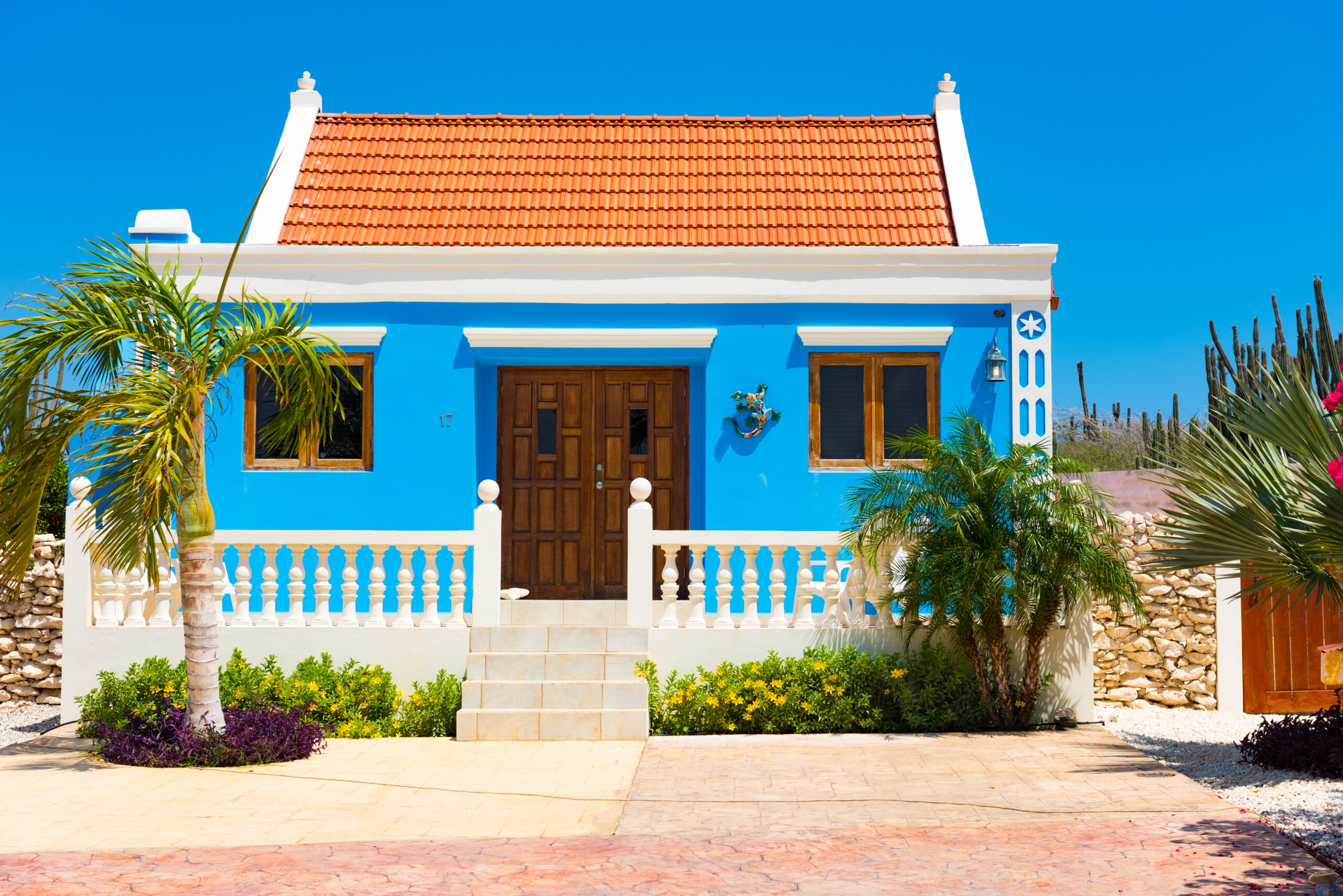 Bright blue Aruban home with a red tile roof and palm trees